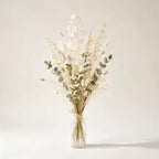Bouquet Mouffetard de fleurs séchées ivoire, sable et vert tendre, présenté dans une bouteille en verre, sur fond crème