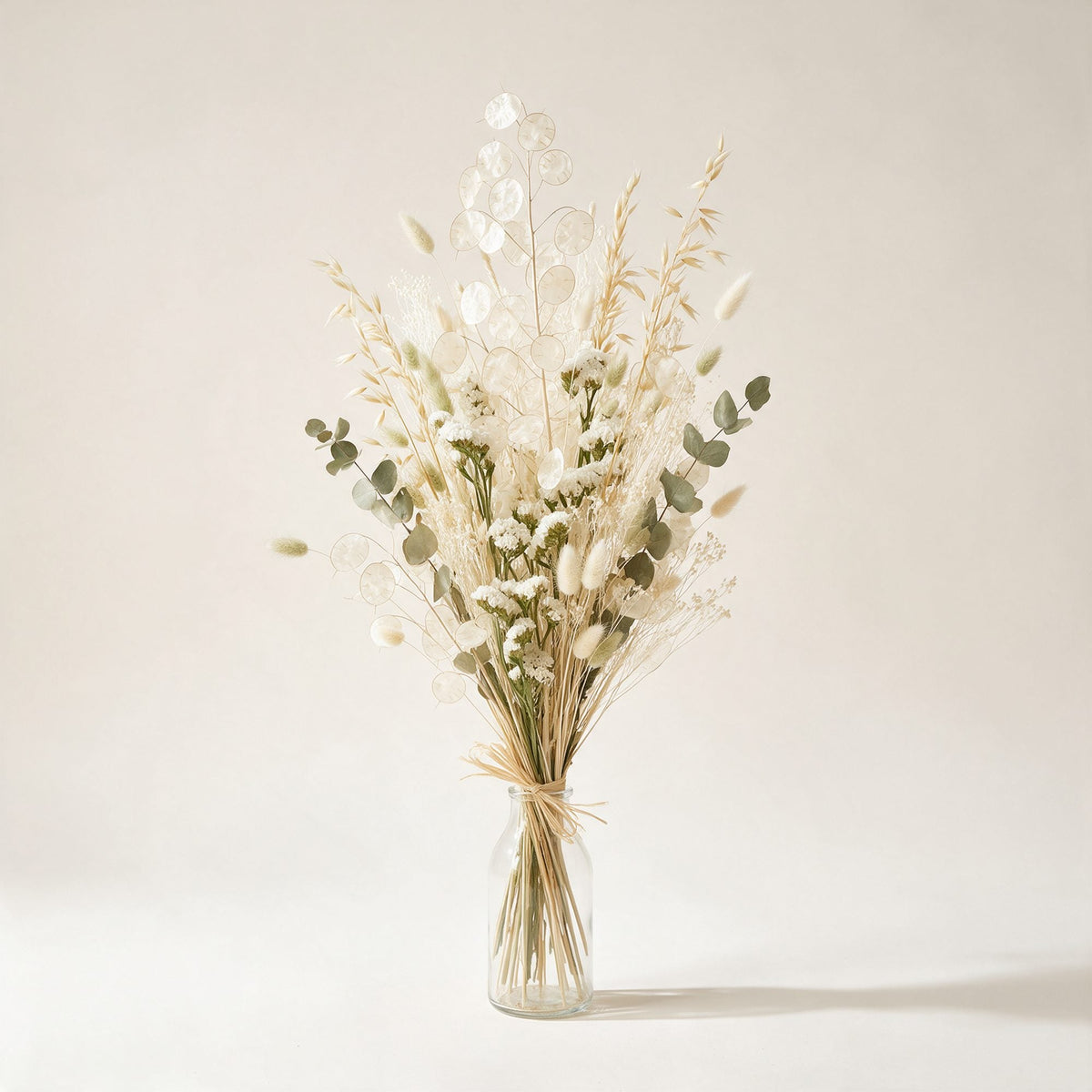 Bouquet Mouffetard de fleurs séchées ivoire, sable et vert tendre, présenté dans une bouteille en verre, sur fond crème