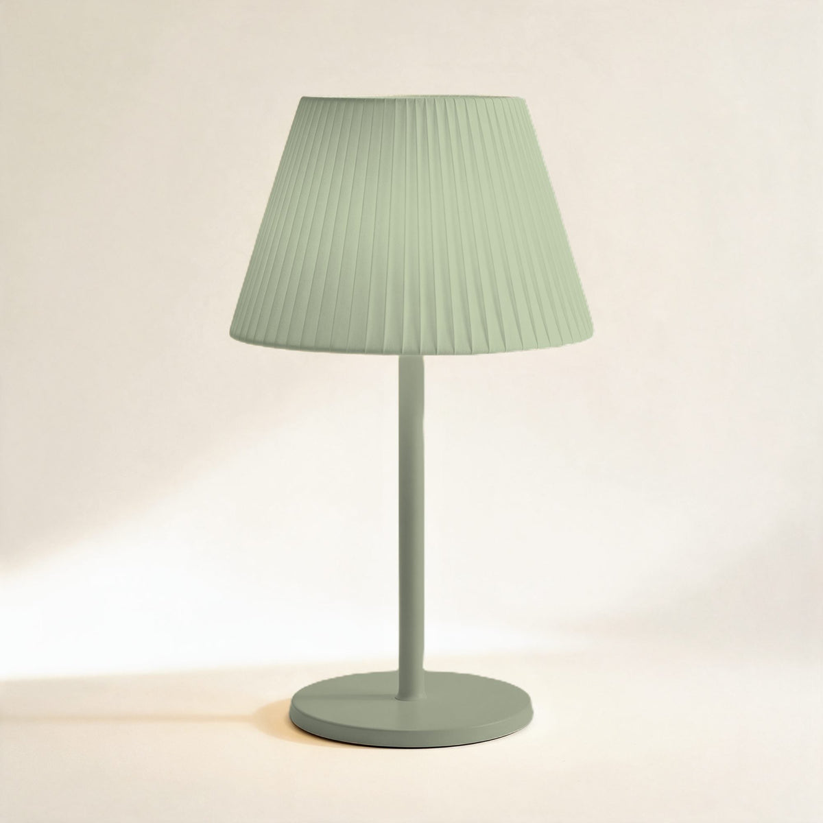 Lampe sans fil Solférino vert sauge à abat-jour plissé, allumée, sur fond crème