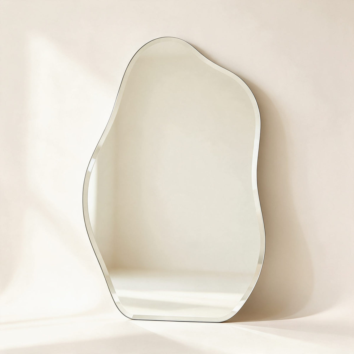 Miroir Orsay sans cadre à la forme organique et au bord biseauté, posé contre un mur crème