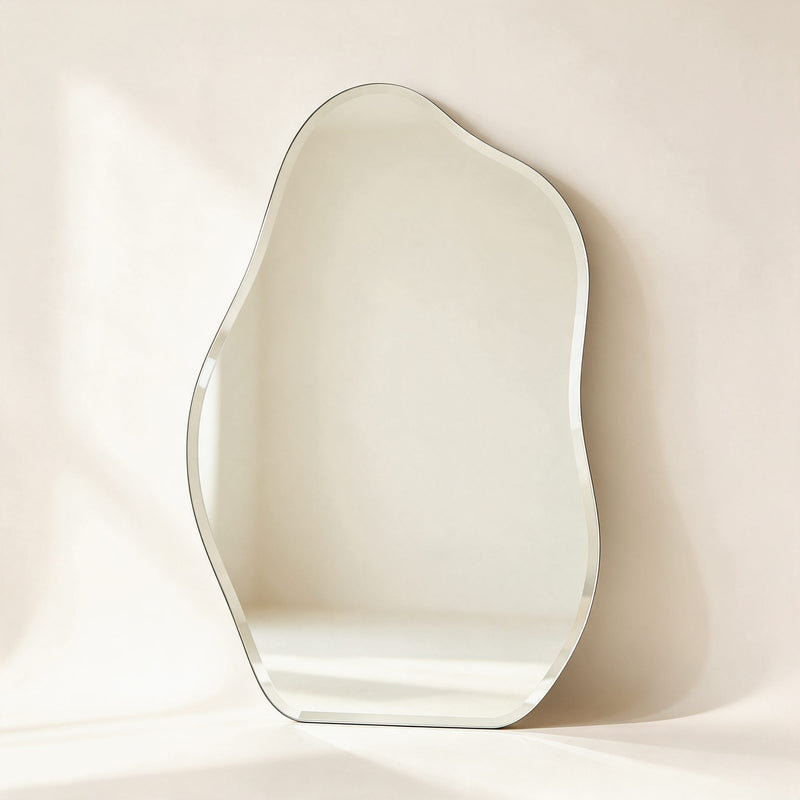 Miroir Orsay sans cadre à la forme organique et au bord biseauté, posé contre un mur crème