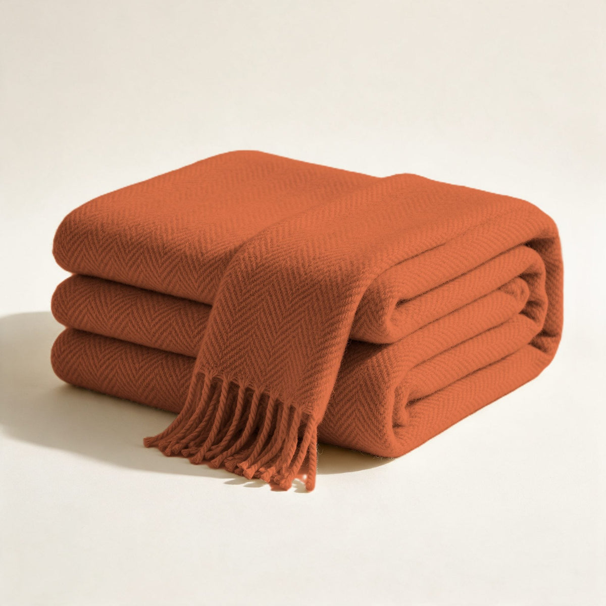 Plaid Cherche-Midi en laine à chevrons terracotta, plié, franges nouées visibles, sur fond crème