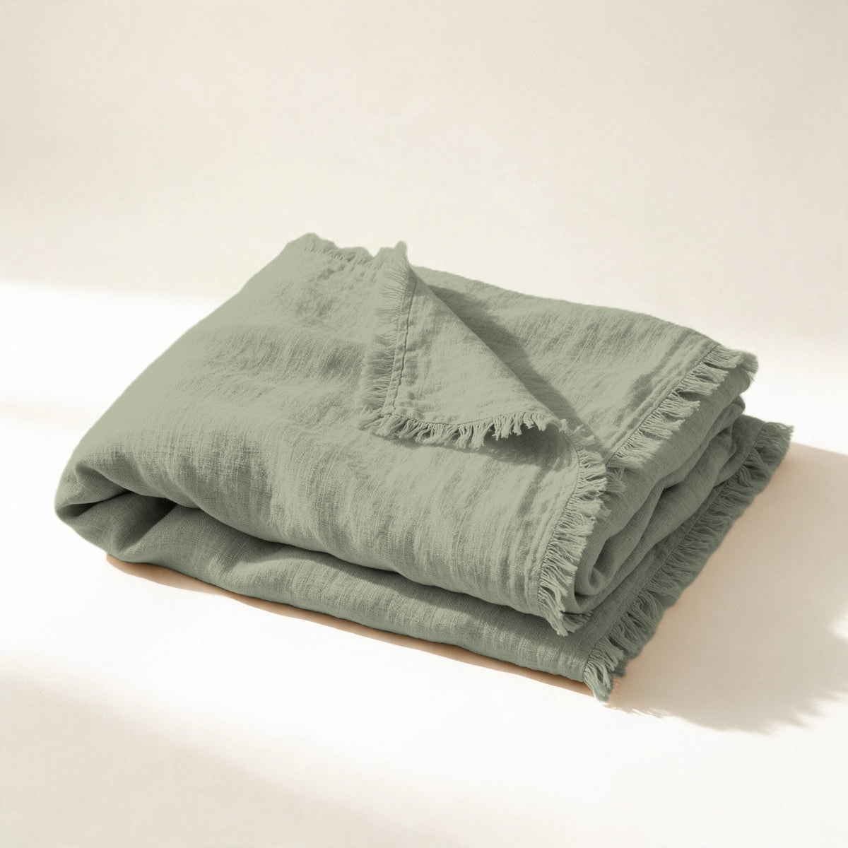 Plaid Varenne en lin lavé vert sauge, plié souplement, franges effilées, sur fond crème