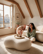 Pouf Nuage en bouclette écrue devant un canapé arrondi, avec un plateau et deux tasses de café ; une femme rit, assise sur le tapis
