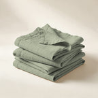 Serviettes de table Buci en lin lavé vert sauge, pliées en pile, sur fond crème