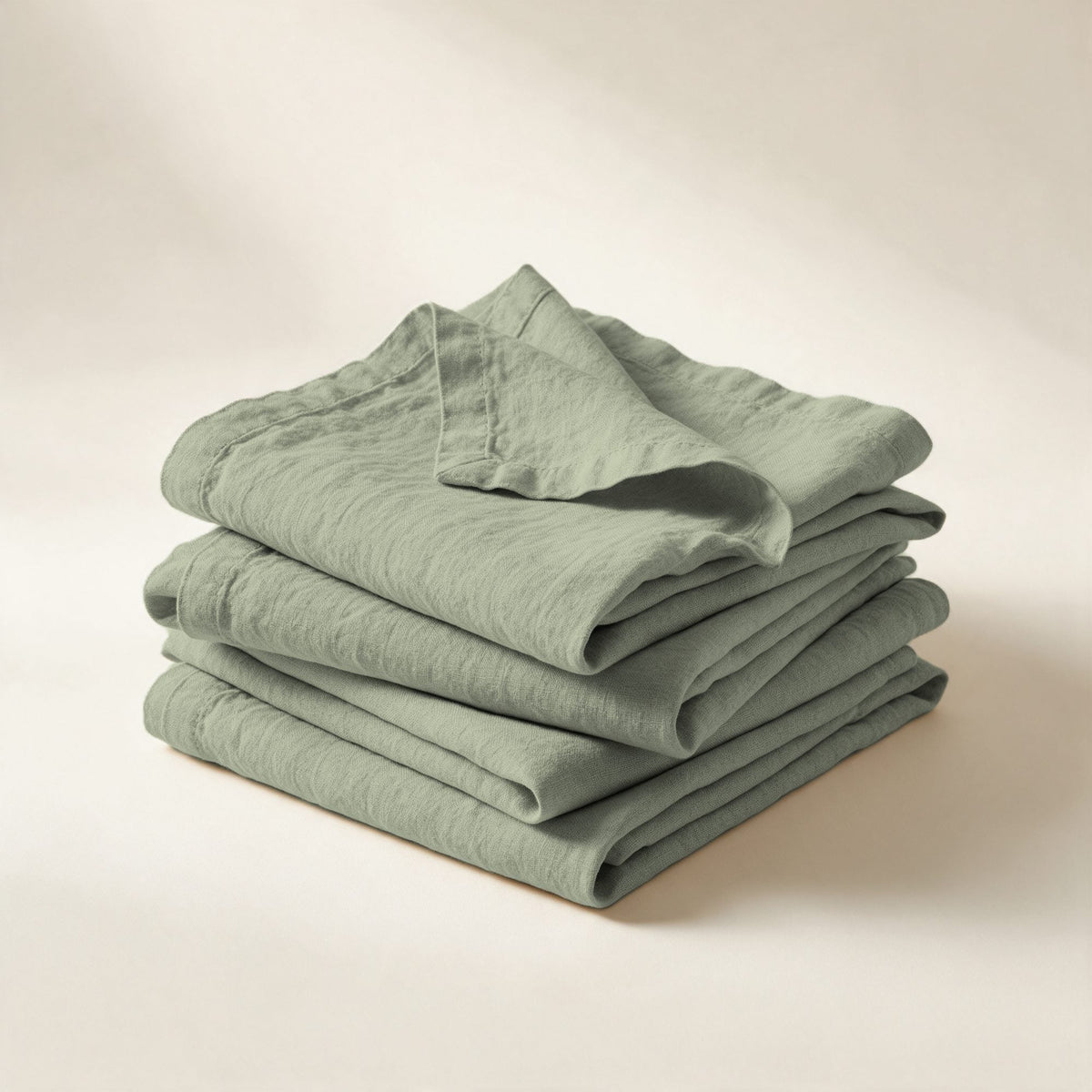 Serviettes de table Buci en lin lavé vert sauge, pliées en pile, sur fond crème
